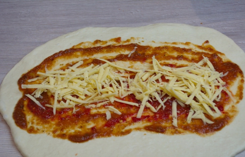 1. Этап. Стромболи: 5. Натрите на терке твердый сыр. Часть сыра мы выложим нижним слоем, а часть — сверху на начинку. Итак, натертый сыр выкладываем на томатный соус. Учтите, что сыр нужно разделить на 3 части, ибо из этого количества теста выйдет 3 пиццы стромболи.