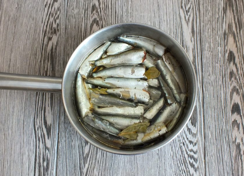 1. Этап. Домашние шпроты из кильки: В сотейник или кастрюлю выложите подготовленную кильку. Сверху раскрошите второй лист лаврушки и добавьте вторую половину перца и гвоздики. Залейте чаем и растительным маслом. Поставьте на огонь. Как только все закипит, убавьте на самый минимальный огонь и варите 1 час 10 минут. Перемешивать не надо! Кастрюлю можно слегка потряхивать.