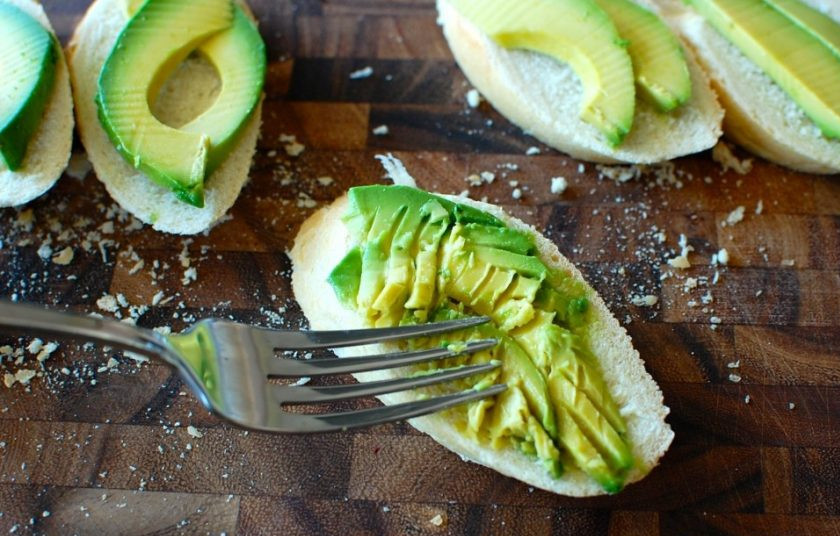 1. Этап. Брускетта с авокадо и томатами: 2. Промойте авокадо, разрежьте его дольками, положите авокадо на ломтики багета, раздавите фрукт на ломтиках с помощью вилки.