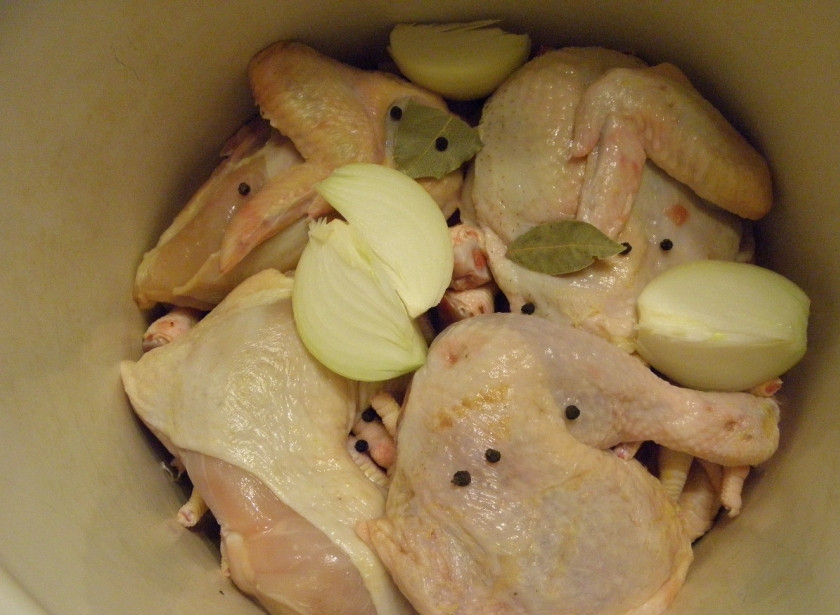 1. Этап. Студень из курицы: Возьмите удобную глубокую кастрюлю, сложите в неё мясо, лавровый лист, перец горошком и очищенную луковицу. Крупную луковицу можно разрезать на 4 части.