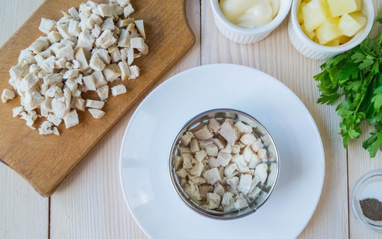 1. Этап. Салат Дамский каприз с курицей: Остывшую куриную грудку нарезаем на мелкие кусочки. И с помощью кольца начинаем формировать салат. Первым слоем выкладываем куриное мясо, посыпаем перцем и слегка смазываем его майонезом.