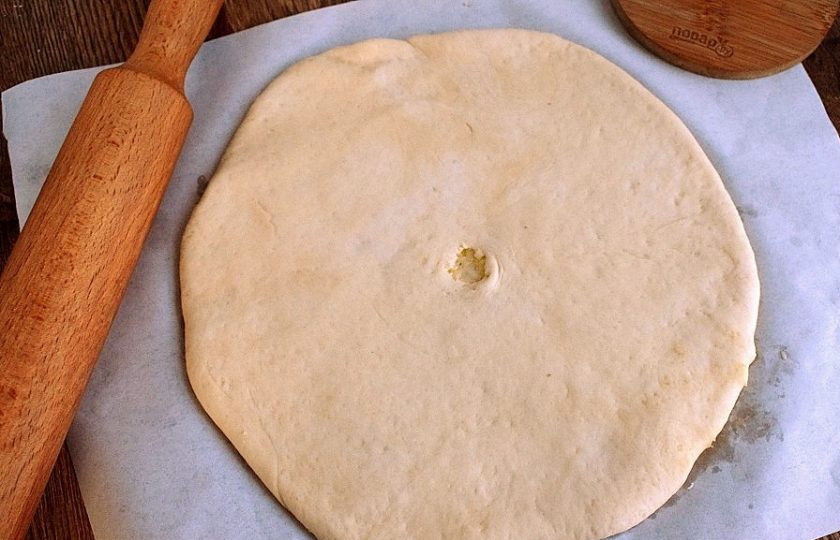 1. Этап. Хачапури по-имеретински классический: Переверните заготовку швом вниз и раскатайте в круглую и максимально тонкую лепешку. В центре сделайте небольшое отверстие, чтобы во время выпечки выходил пар.