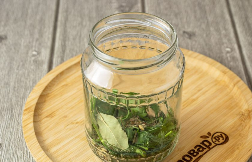 1. Этап. Соленые огурцы хрустящие: На дно банки положите крупно порубленную зелень, очищенный чеснок и все специи.