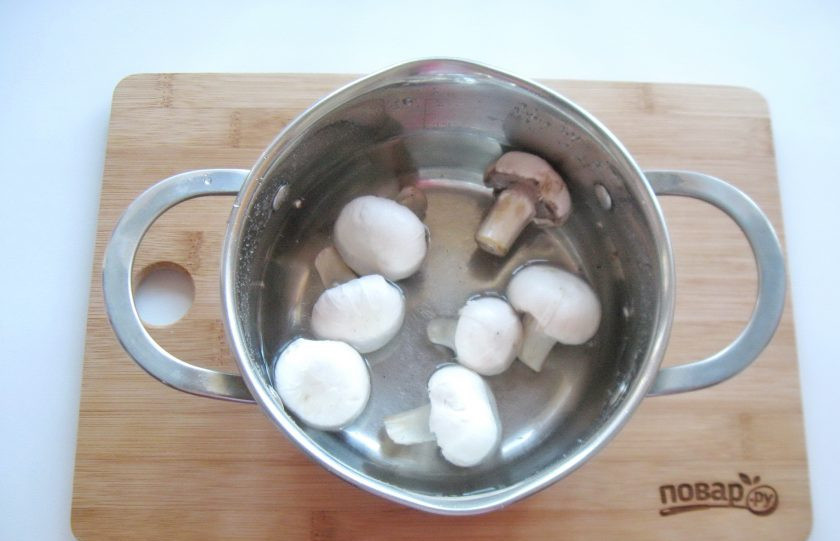 1. Этап. Салат Мошенница: Шампиньоны очистите, выложите в кастрюлю и залейте водой. Варите 7-8 минут с момента закипания. После достаньте грибы из кастрюли, охладите и нарежьте.