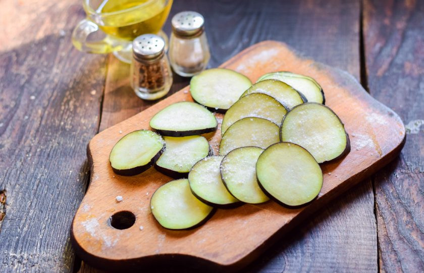 1. Этап. Хрустящие баклажаны с помидорами и кинзой: Баклажан сполосните и просушите, нарежьте тонкими пластинами. Посыпьте баклажаны солью, оставьте на 5 минут, после промойте и просушите.