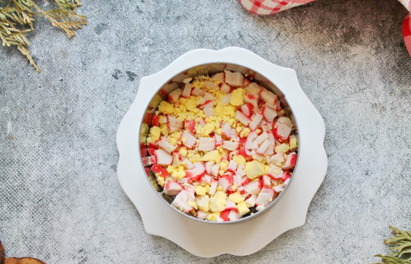 1. Этап. Салат Черное море: Отварное яйцо почистите и разделите на белок и желток. Крабовые палочки и желток порежьте мелким кубиком, перемешайте. Выложите их на морскую капусту и нанесите майонезную сеточку.