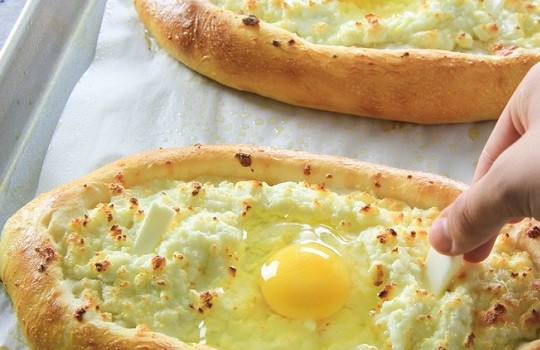 1. Этап. Хачапури по-грузински с сыром: 12. В центре каждой лодочки сделайте аккуратно ложкой небольшое углубление, вбейте по 1 яйцу. Также можно добавить по 1-2 кусочка сливочного масла.