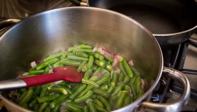 1. Этап. Суп из стейка семги: 1. Очистите лук, затем нарежьте его небольшими кубиками. Вымойте стручковую фасоль, обрежьте края. В кастрюле разогрейте кокосовое масло, выложите луковицу и стручковую фасоль. Перемешайте лопаткой и обжаривайте несколько минут.