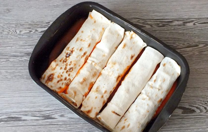 1. Этап. Энчиладос с курицей в лаваше: На дно формы налейте 1/4 часть приготовленного соуса. Выложите подготовленные рулетики с фаршем.