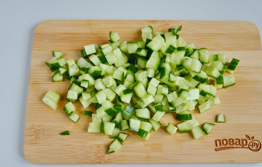 1. Этап. Слоеный салат из хурмы: Огурчик порежьте кубиками.