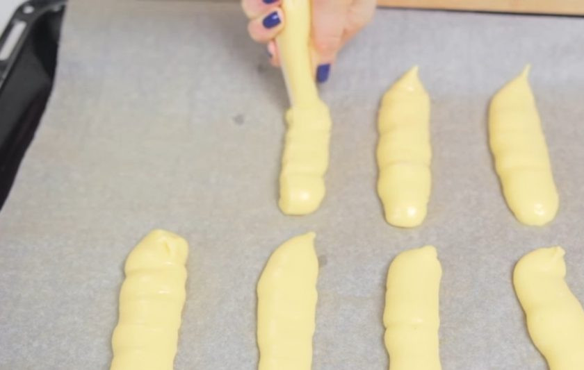 1. Этап. Простые эклеры: 5. С помощью кондитерского мешка высадите эклеры длинной 5-6 см на застеленный пергаментной бумагой противень, оставляя место между ними.