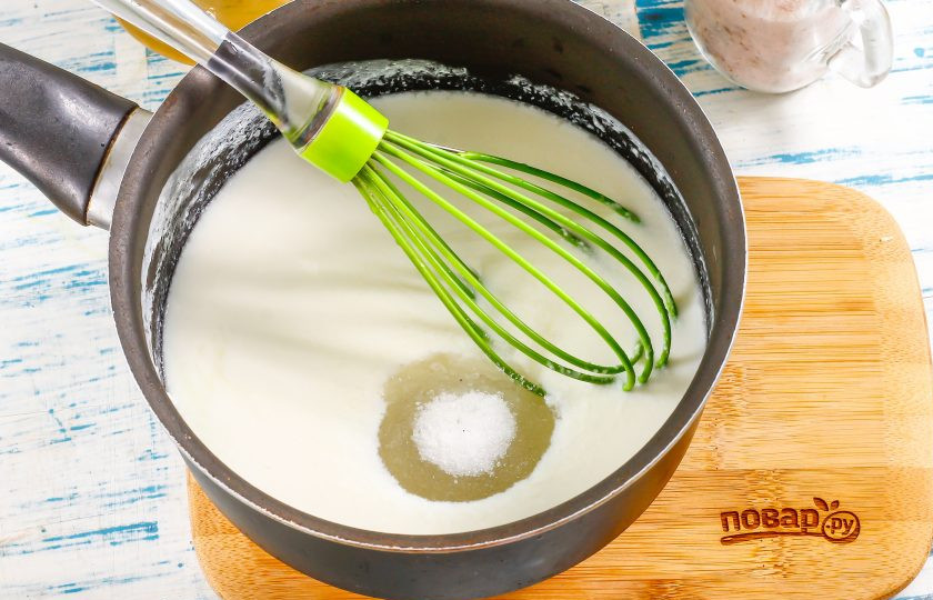 1. Этап. Толстые блины без дрожжей: Перелейте в ковш с антипригарным дном или казанчик кефир любой жирности, прогрейте его, но не до кипения. Жидкость должна быть теплой. Всыпьте в нее сахар, соль и ванильный сахар, перемешайте. Если используете силиконовый венчик, то можно готовить тесто прямо в емкости, если железный, то перелейте кефир в миску.