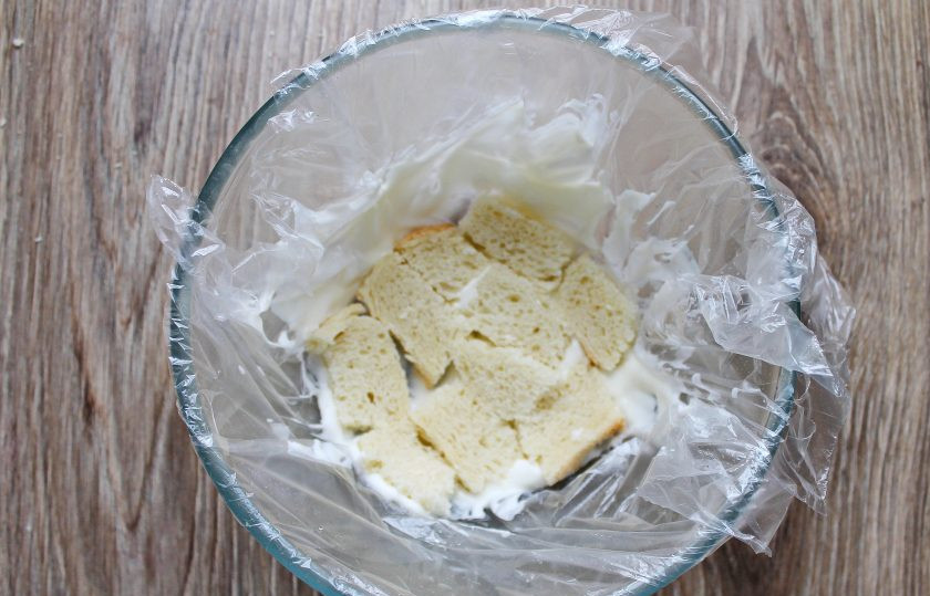 1. Этап. Торт без выпечки из батона: Полукруглую форму ополосните и застелите пленкой. Смажьте дно и бока сметаной массой, и плотно выложите кусочки батона в один слой.