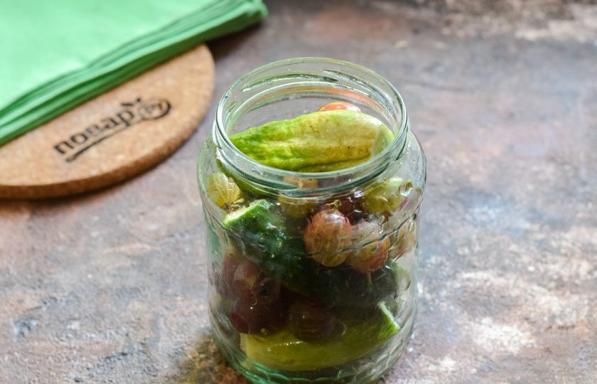 1. Этап. Огурцы с крыжовником на зиму: Наполните банку огурцами и крыжовником. Банку пару раз стряхните, чтобы все ингредиенты плотно легли друг к другу.