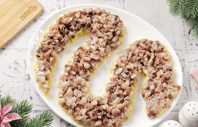 1. Этап. Селедка под шубой на год Змеи 2025: Поверх картофеля выложите филе сельди, нарезанное кубиками. Смажьте слой майонезом.