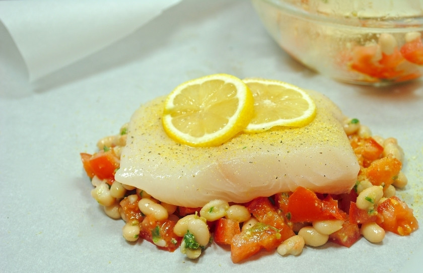 1. Этап. Палтус с овощами в духовке: Выложите поверх смеси бобов и помидор кусочек палтуса, посыпьте его перцем и положите сверху два ломтика лимона.