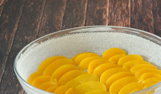 1. Этап. Сочный пирог с консервированными персиками: Форму смажьте маслом и посыпьте манкой. При чем посыпайте манкой только бортики формы, чтобы манка не отпечаталась на персиках. Можно выстелить форму пергаментом для выпечки, что поможет вам легче извлечь потом пирог из формы. Размер моей формы 20*30 см. Консервированные персики нарежьте дольками и выложите на дно формы.