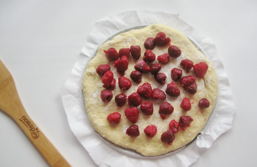 1. Этап. Дрожжевой пирог с малиной: Разделите тесто на две части. Одну часть раскатайте в пласт и выложите в форму для выпекания. У меня форма диаметром 22 сантиметра со съемными бортиками. В данном случае удобно снять бортики. Посыпьте тесто крахмалом, чтобы он впитал сок от ягод. Выложите малину. Мороженую малину не размораживайте.