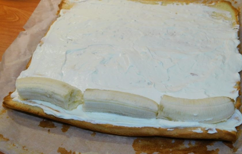 1. Этап. Бисквитный рулет с бананом: Остывший рулет отсоедините от бумаги. Распределите по нему крем. Положите очищенный банан и скрутите в рулет.