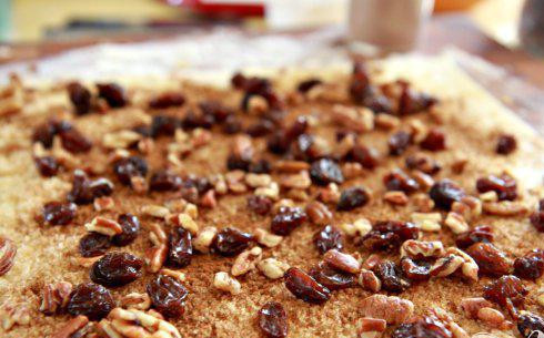 1. Этап. Булочки с орехами и изюмом: 2. Слегка посыпать мукой рабочую поверхность. Развернуть 1 лист слоеного теста. Смазать весь лист растопленным сливочным маслом. Оставив границы по 2,5 см по краям, посыпать лист теста 1/3 стакана коричневого сахара, 1 1/2 чайной ложки корицы, 1/4 чашки пекан и 1/4 чашки изюма.