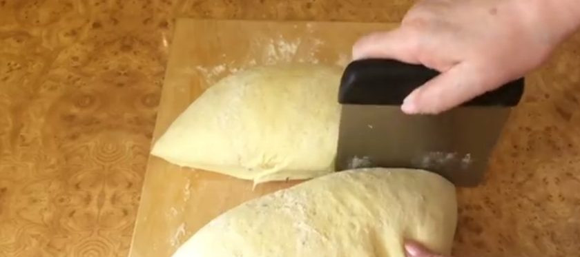 1. Этап. Пшеничный калач Солнышко: 4. Повторите растягивание по кругу, после чего переверните тесто, выровняйте его поверхность и оставьте под пленкой до конца расстойки. Выложите тесто на присыпанную мукой рабочую поверхность, округлите и разделите на 2 части.