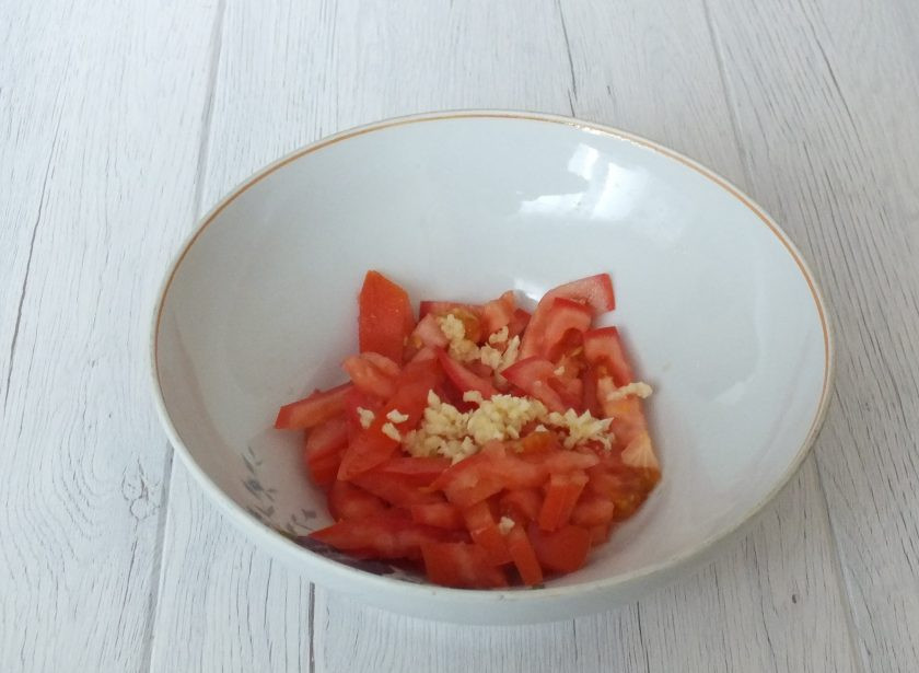 1. Этап. Салат Красное море с кальмарами: Нарежьте помидоры крупной соломкой. Переложите в салатник. Добавьте измельченный чеснок и посолите. Перемешайте.