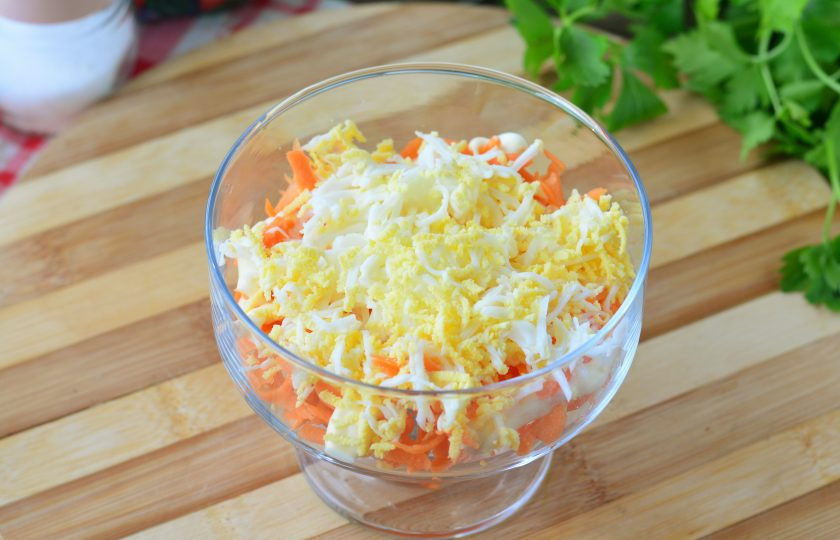 1. Этап. Салат Кудрявый с крабовыми палочками: Сварите куриные яйца вкрутую, почистите и натрите на терке, выложите вторым слоем натертые яйца. Немного посолите.