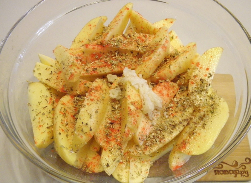 1. Этап. Картошка по-деревенски в духовке: В картофель добавьте пропущенные через пресс чеснок, орегано, паприку, соль, перец. Тщательно руками перемешайте картофель.