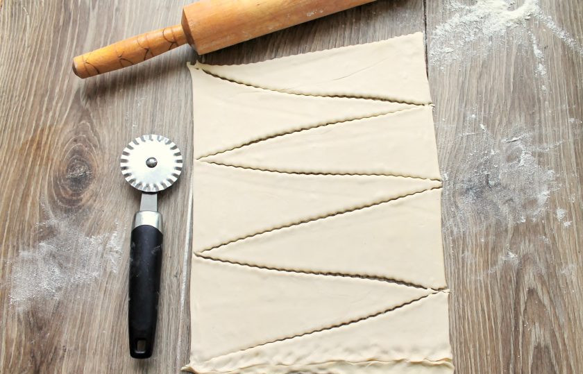 1. Этап. Круассаны с черникой: Раскатайте тесто в одном направлении толщиной 0.5 миллиметра. Разрежьте его на треугольники. Крайние части соедините по прямой линии, чтобы получился еще один полноценный треугольник.