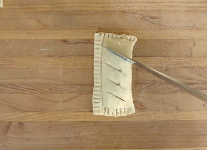 1. Этап. Яблочные слойки с корицей: 7. По желанию немного присыпьте слойки сахаром. Сделайте сверху несколько надрезов на тесте.