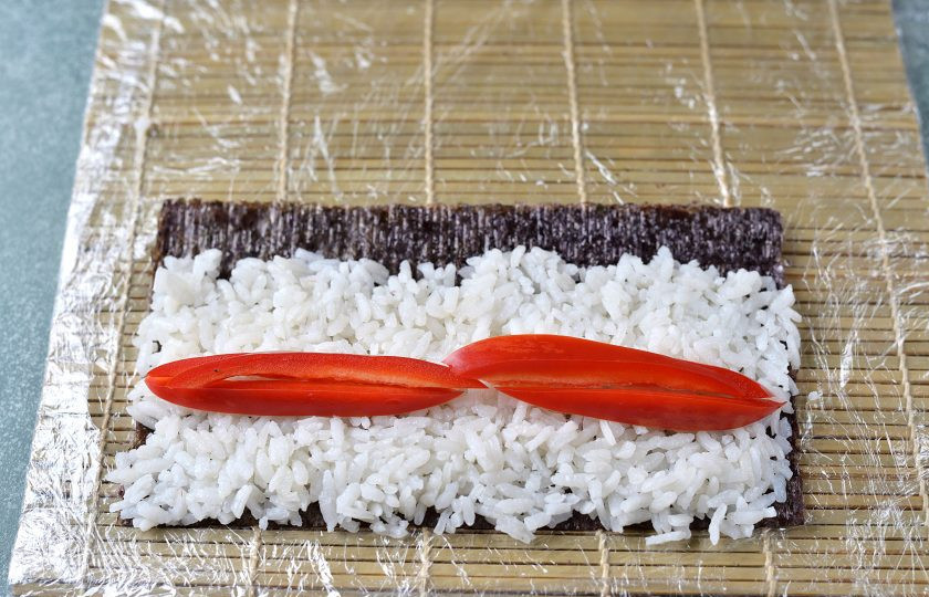 1. Этап. Роллы с болгарским перцем: Лист нори разрежьте пополам, выложите слой риса, оставив дальний край нори свободным. Выложите посередине несколько ломтиков болгарского перца.