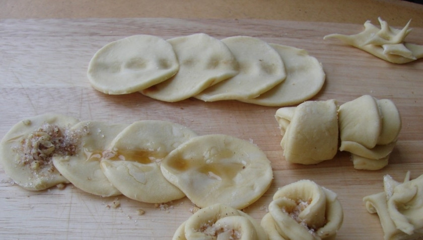 1. Этап. Печенье Розочки с орехами: 2. Тесто разворозим, вырежем из него кружочки. Сложите их внахлест по 4 шт. и придавите пальцем по центральной линии. Промажем мёдом, на первый круг выложим начинку, скатаем тесто рулетом. Дальше посередине изделия надавим пальцем, разделим пополам. Срез защипнем.