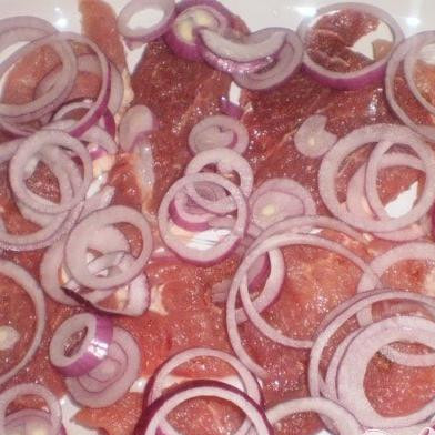1. Этап. Мясо с грибами и помидорами: 1. В первую очередь приготовим все продукты. Очищаем лук, в проточной холодной воде промываем мясо. Примерно толщиной один сантиметр нарезаем мясо ломтиками, можно отбить обратной стороной ножа или молоточком. Смазываем форму растительным маслом и выкладываем на нее мясо. Приправляем мясо специями и солим. Кольцами нарезаем лук и выкладываем на мясо.