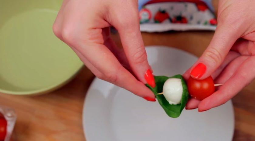 1. Этап. Канапе с черри и моцареллой: 2. Затем на зубочистку или шпажку оденьте помидор черри, затем прикрепите один край листика шпината. После этого оденьте на шпажку шарик моцареллы и опять заверните листик шпината.