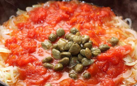 1. Этап. Рыбная солянка с семгой: 4. Очищаем лук и нарезаем его тоненькими полукольцами. В сковороде на растительном масле пассируем его до прозрачности. Помидоры и каперсы нарезаем маленькими кубиками и добавляем в лук. Минут пять готовим на не сильном огне, помешиваем.