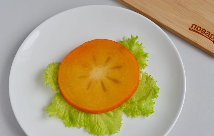 1. Этап. Слоеный салат из хурмы: На тарелку уложите вымытые молоденькие листья салата, сверху колечко хурмы.