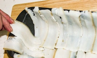 1. Этап. Паштет из куриной печени в духовке: Подмороженное сало нарежьте тонкими ломтиками. Уложите их на дно и бока формы для запекания внахлёст. Печень заранее промойте и положите в молоко на 1 час.