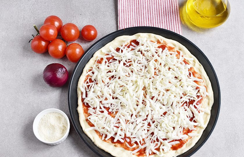 1. Этап. Пицца с шампиньонами: Посыпьте основу пиццы тертой моцареллой, раскладывая ее ровным слоем.