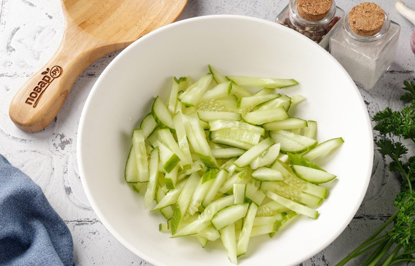 1. Этап. Салат с кукурузой, огурцом и сыром: Огурец промойте, нарежьте небольшой соломкой и переложите в салатник или глубокую миску.