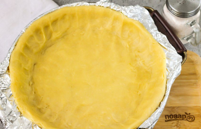 1. Этап. Сметанник из песочного теста: Разогрейте духовку до 180 градусов и выложите в форму для запекания песочное тесто, распределите его руками, заходя на бортики. Поместите форму в духовку и запеките тесто 15 минут.