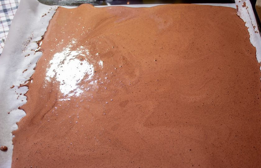 1. Этап. Шоколадный рулет без муки: Тесто вылейте на противень, выстеленный пергаментом с силиконовым покрытием. Выпекайте в разогретой духовке до 180 градусов 13-15 минут.