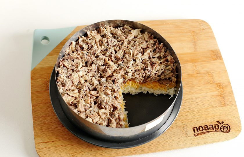 1. Этап. Салат Мышиная радость: С консервов слейте жидкость, удалите крупные косточки и хорошо разомните их вилкой. Выложите консервы поверх сыра.