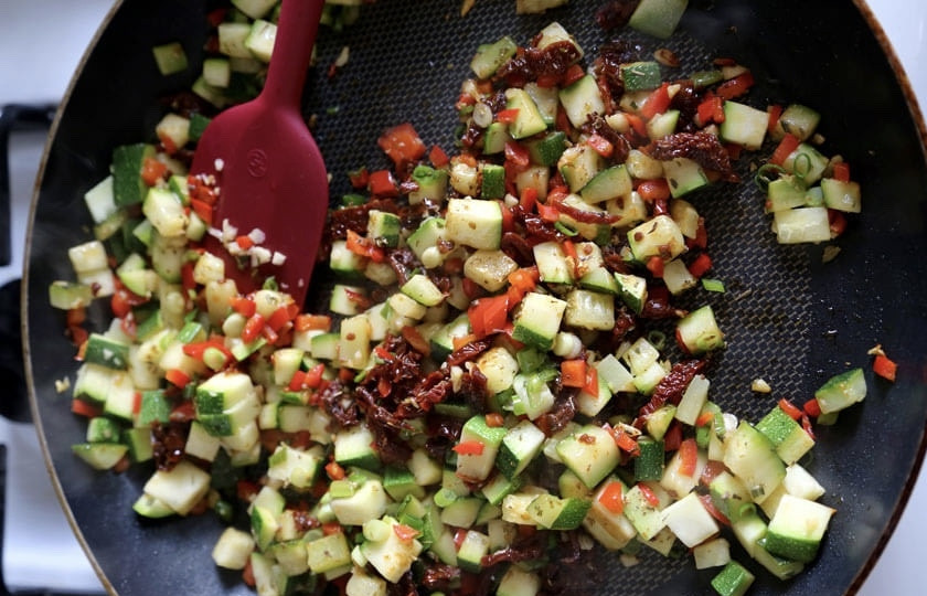 1. Этап. Солёная домашняя выпечка: Разогрейте сковороду с оливковым маслом. Добавьте пропущенный через пресс чеснок. Также добавьте розмарин и нарезанные кубиками перец и цукини. Обжаривайте на среднем огне 4 минуты. Затем добавьте тонко нарезанные вяленые помидоры. Обжаривайте еще минуты 3 и переложите готовые овощи на тарелку.