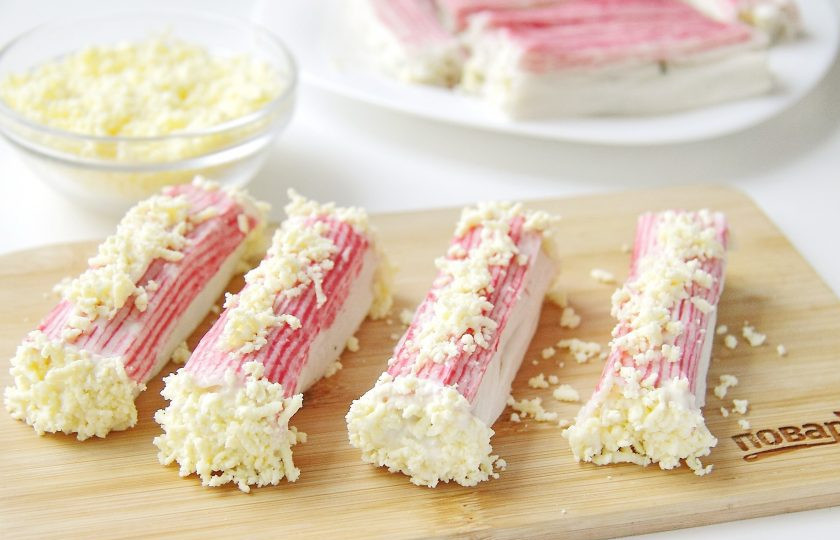 1. Этап. Новогодние рулетики из крабовых палочек: Каждую палочку с двух сторон обмакните сначала в майонез, а затем в тертые желтки. Сверху также немного смажьте палочки майонезом и украсьте желтком.