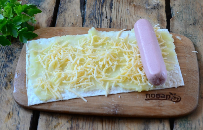 1. Этап. Сосиски в картофельно-сырной шубке: На первый кусок лаваша намажьте картофельное пюре тонким слоем, сверху присыпьте сыром, натертым на мелкой терке. С одного края положите сосиску, заверните лаваш вместе с начинкой в рулет.