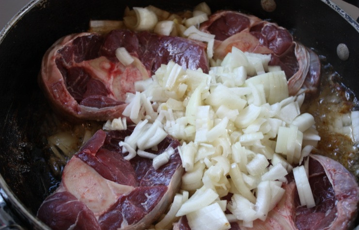 1. Этап. Суп из чечевицы с копченостями: 1. Приготовьте все овощи для супа. Почистите и нарежьте кубиками лук, морковь. Промойте и измельчите зелень. Картошку и колбаски мы нарежем позже. Голяшки промойте и выложите в кастрюлю с маслом на средний огонь. Обжарьте слегка с двух сторон, пока мясо не поменяет цвет. Затем добавьте нарезанный лук. Жарьте до мягкости.