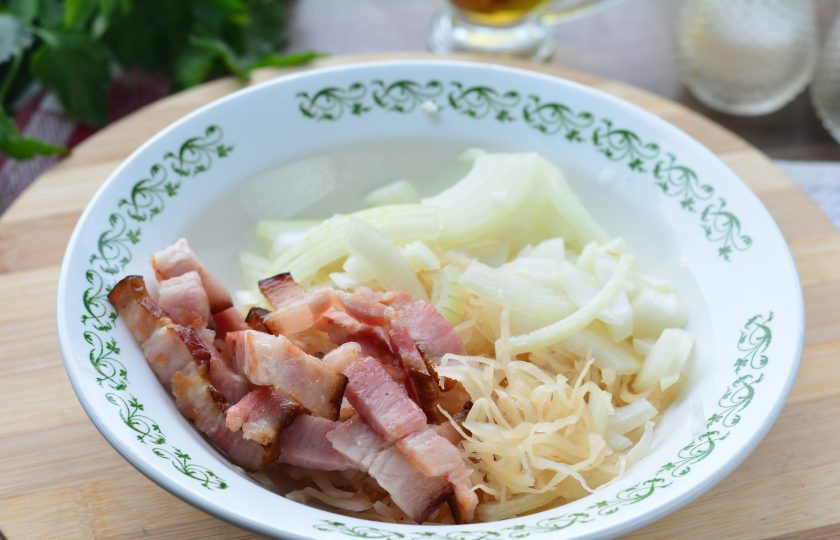 1. Этап. Салат с квашеной капустой и жареным беконом: В глубокой тарелке смешайте капусту, лук и жареный бекон.