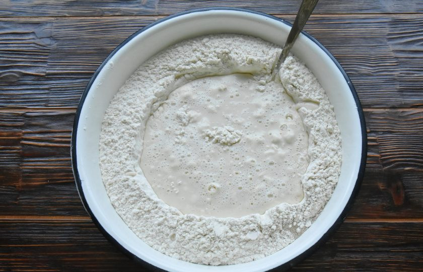 1. Этап. Пигоди по-корейски: В центре горки с мукой сформируйте углубление и влейте в воронку теплую воду. С помощью вилки замесите тесто, подсыпая в жидкость муку с краев воронки.