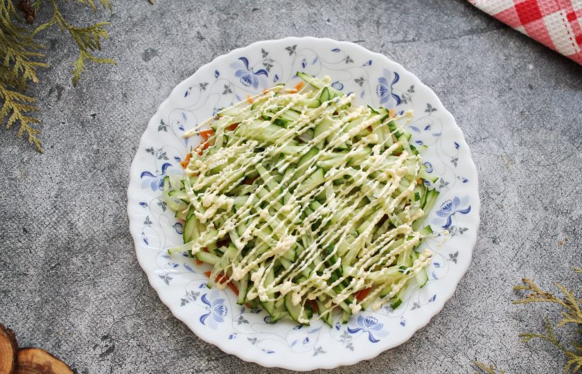 1. Этап. Салат Орхидея с чипсами и ветчиной: Огурец порежьте тонкой соломкой и выложите поверх моркови по-корейски. Сделайте сверху сеточку из майонеза.