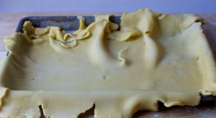 1. Этап. Ленивый киш со шпинатом: Раскатайте тесто в тонкий пласт, застелите им смазанный маслом противень. Аккуратно сформируйте бортики. Натрите на терку сливочный сыр, распределите его по тесту.